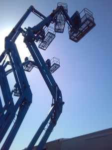 three Genie boom lift booms with sun behind